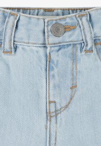 Lys blå denimstof med en knaplukning og orange syninger. Har en talje og bæltesløjfer, med en blød tekstur.