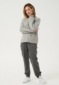 Pulover gri deschis, cu o croială lejeră și mâneci lungi, asortat cu pantaloni tapered gri închis și adidași albi. Textură moale, design minimalist.