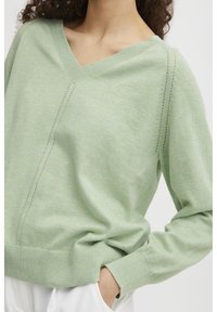 Helles grünes V-Ausschnitt-Pullover aus weichem Material. Verfügt über einen gerippten Saum und Bündchen sowie über subtile gestickte Details an den Schultern.
