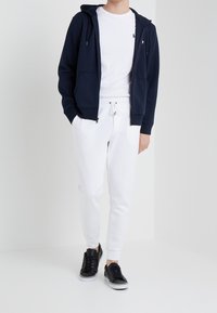 Marinblå zip hoodie, vit t-shirt, vita sweatpants och svarta sneakers. Mjukt tyg, tajt design, med dragsko i midjan och fickor.