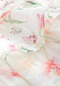 Durchsichtiger Stoff mit einem floralen Muster aus rosa und pastellfarbenen Blumen, grünen Blättern und zarten Schmetterlingen. Mit einem Gittermuster strukturiert.