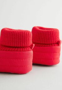 Røde hjemmesko med strikket kant og en glat, polstret sål med subtile stikningsdetaljer. Både materiale og farve er ensartede.
