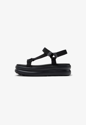 Black sandals featuring a thick, textured sole, adjustable nylon straps, and a minimalistic design. No visible logos or patterns.