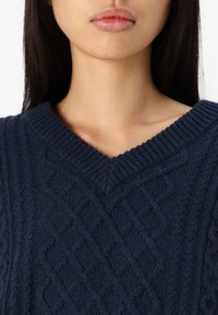 Granatowy sweter dziany z dekoltem w serek i teksturowanym wzorem w warkocze, z grubymi ściągaczami przy mankietach i kołnierzu dla dodatkowego wykończenia.