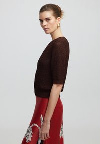 Suéter marrón de punto con mangas cortas y acabado texturizado, combinado con una falda roja con estampados florales en blanco y negro, mostrado de perfil.
