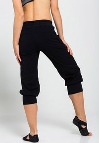 Černé zkrácené kalhoty s pohodlným pasem a ohrnutými lemy. Materiál působí měkce a pružně. Nošeny s černou lehkou obuví.