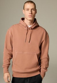 Hooded sweatshirt in dusty rose color, cotton blend, featuring a front pocket and drawstring hood with metallic tips. Smooth texture.