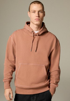 Sudadera con capucha en color rosa polvo, mezcla de algodón, con un bolsillo frontal y capucha con cordón ajustable con puntas metálicas. Textura suave.