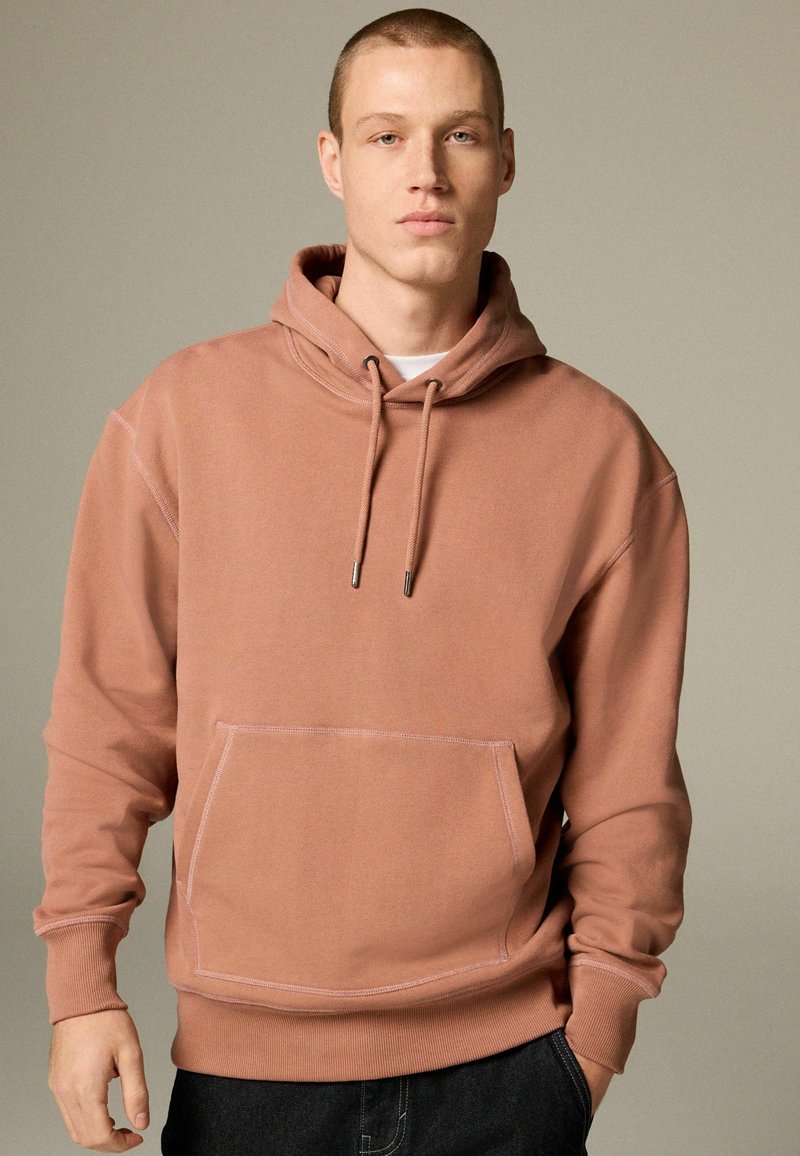 Hooded sweatshirt in dusty rose color, cotton blend, featuring a front pocket and drawstring hood with metallic tips. Smooth texture.