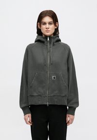 Sudadera gris con cremallera y cuello alto, bolsillos frontales y puños acanalados. Presenta un parche de logo en el bolsillo izquierdo. Tejido suave y texturizado.