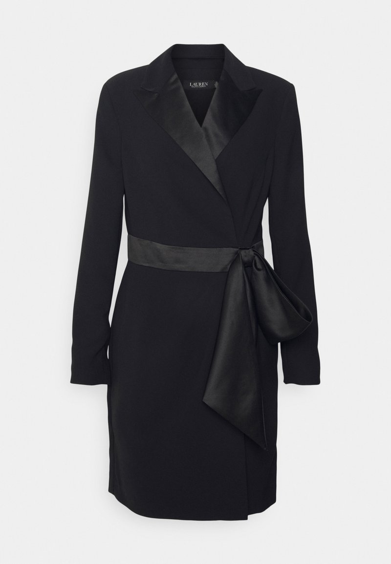 Musta nylonnimekko pitkillä hihoilla, satiinikoristeilla, suurella solmupuskalla ja klassisella kauluksella. Sujuva materiaali, jossa on tarkasti muotoiltu siluetti.