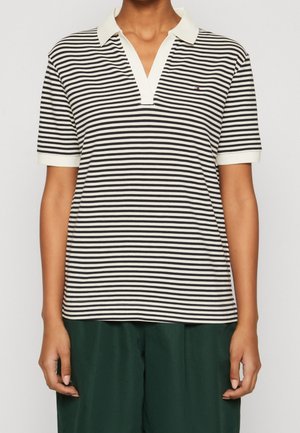Personne portant un polo à rayures horizontales noires et blanches, manches courtes, avec un col blanc et un pantalon vert foncé.