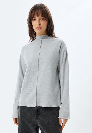 Grijze blouse met lange mouwen en hoge kraag, met een middennaad en een onafgewerkte zoom. Het materiaal lijkt zacht, met een losse, boxy pasvorm.