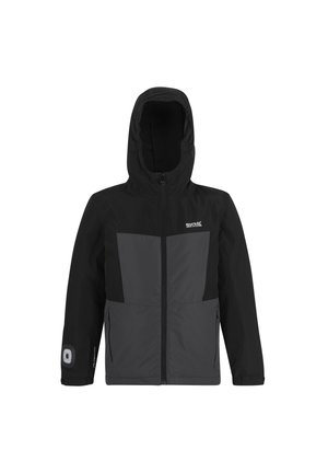 Uśmiechnięty chłopiec w mundurku szkolnym, ubrany w czarno-szarą kurtkę z kapturem, białą koszulę, paskowany krawat, szare spodnie i czarne buty, stojący.