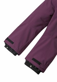 Skidjackans ärmar i djupt lila tyg, med elastiska muddar, kardborreband och svarta detaljer i ändarna för en säker passform och isolering.