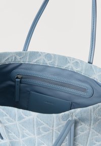 Τσάντα tote ανοιχτό γαλάζιο με υφή εξωτερικά που απεικονίζει γεωμετρικά σχέδια, λείο εσωτερικό και τσέπη με φερμουάρ για ασφαλή αποθήκευση.