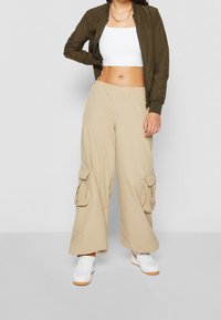 Olivgrön bomberjacka, vit crop top, beige cargobyxor med sidofickor och vita sneakers med orangea accenter.