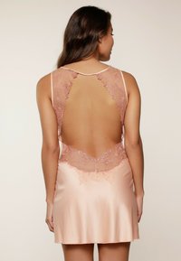Abito in satin di un rosa tenue con schiena scoperta e dettagli in pizzo intricati in un motivo floreale sul collo e sulla schiena. Tessuto morbido.