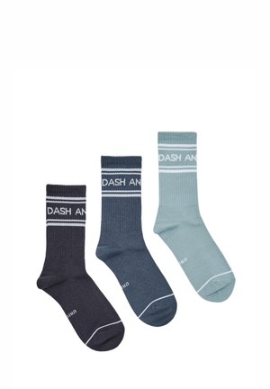Trois paires de chaussettes côtelées type crew en noir, bleu foncé et bleu clair avec des rayures blanches et un texte partiel près du bord-côte.