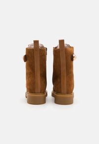 Botas de tobillo de ante marrón con un acento de cuero suave, una suela de goma resistente y un detalle decorativo de botón en el costado.