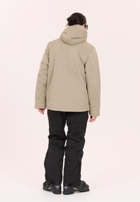 Beige isolerad jacka med huva, tillsammans med svarta byxor och texturerad yta. Designen inkluderar enkla linjer och en rak passform.