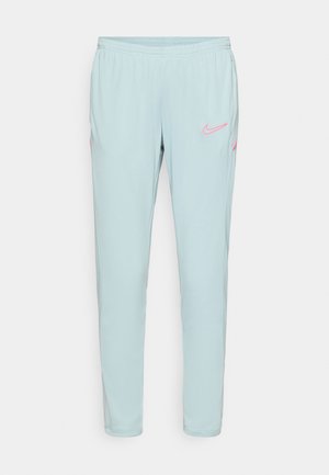 Pantaloni de trening Nike de culoare albastră deschisă, cu o textură netedă, talie elastică și accente roz ale logo-ului pe coapsa stângă și pe buzunare.