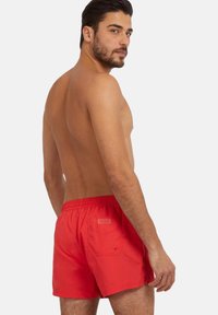 Bañador rojo con cintura elástica y bolsillo trasero. Fabricado con material ligero, presenta un diseño limpio y acentos mínimos.