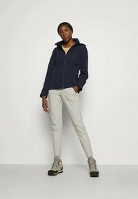 Tumesinine vetthüoodiga jakki, mis on harmooniliselt kombineeritud heledate hallide pükstega ja beežide matkasaabastega. Jakk omab siidist ja sujuvat tekstuuri.