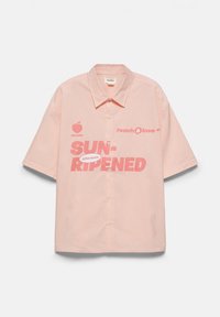 Chemise rose clair à manches courtes avec fines rayures blanches et texte rose indiquant "SUN-RIPENED," "Peach & love," ainsi qu'un petit graphique de pêche.