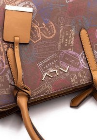 Sac à main marron à motif avec des graphiques sur le thème du voyage, des accents en cuir beige et du matériel en métal. Dispose de doubles anses et d'une fermeture éclair.