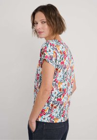 Trumpas rankovės gėlėtas marškinėliai iš medvilnės. Su daugiaspalvėmis gėlėmis ant šviesaus fono, apvaliu iškirpimu ir laisvu siluetu.