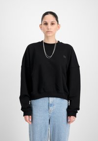 Felpa nera con scollatura a girocollo, spalle scese e un piccolo patch logo. Abbinata a jeans baggy blu chiaro. Texture del tessuto liscia.