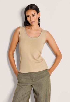 Beige geribbelde tanktop met een ronde hals en zilveren rand. Gepaarde met een broek in een groen patroon, met een textuur in herringbone-design.