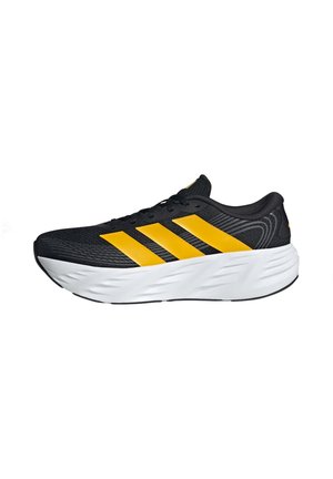 Černá běžecká bota s třemi výrazně žlutými pruhy a silnou bílou polstrovanou podrážkou, boční pohled na bílém pozadí.
