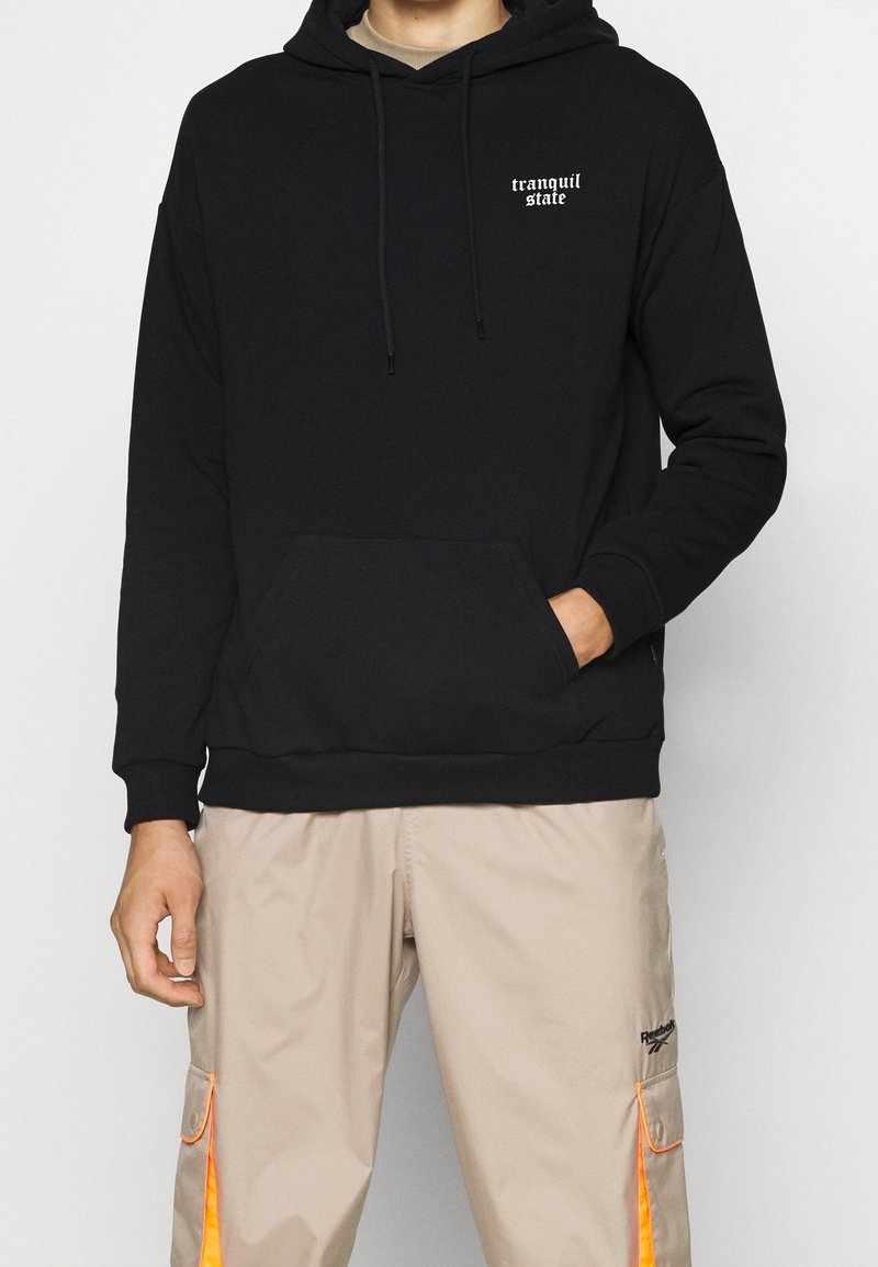 Sudadera negra con bolsillo canguro delantero, capucha ajustable con cordones y texto blanco que dice "estado tranquilo". Fabricada en tela suave.