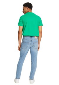 Un tricou verde cu maneci scurte, asortat cu blugi deschis la culoare, cu un design clasic cu cinci buzunare. Tenisi albi completează ținuta.