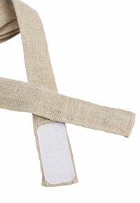 Beežikas kangast rihm kareda tekstuuriga, mille ühes otsas on ristkülikukujuline valge takjapaelakinnitus.