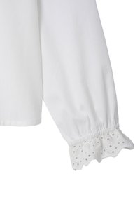 White cotton blouse with long sleeves, featuring a gathered cuff with scalloped eyelet trim and perforated floral designs.