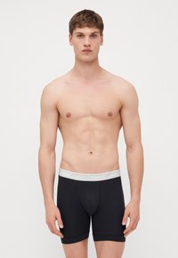 Sorte bokserer med et hvidt Nike-logo på den elastiske livlinje. Lavet af et glat, strækbart stof, designet med en tætsiddende form.