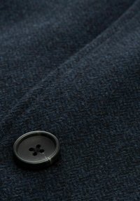 Tela de un azul marino oscuro con una textura tejida, que presenta un botón negro redondo con cuatro agujeros. El botón está destacado en la tela.
