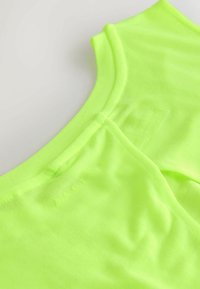 Haut vert néon en tissu doux et extensible. Il présente un col arrondi et une texture lisse avec un détail discret de la marque près du col.