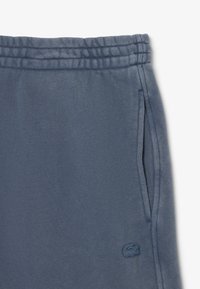 Pantaloni felpati blu in cotone con vita elastica, tasche laterali e un piccolo logo ricamato in basso a sinistra. Texture morbida.