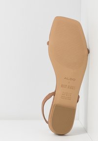 Vaaleat sandaalit, joissa on sileä, litteä pohja, merkitty "ALDO" ja "ROCKY BARNES". Omistaa ohuet hihnat ja ribatoituneen pinnan pohjassa.