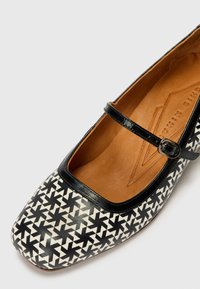 Black and white patterned flat shoe with a square toe, leather exterior, and a black strap across the instep. Smooth tan interior lining.