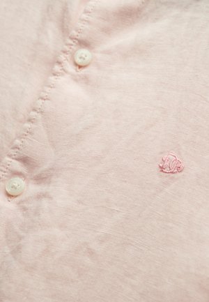 Lichtroze linnen overhemd met kleine witte knopen en subtiele geborduurde logo in roze draad. Glad textuur met een lichte glans.