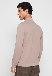 Lichtbeige sweatshirt met een hoge kraag en geribde zoom, met een gladde textuur en lange mouwen, gezien vanaf de achterkant.