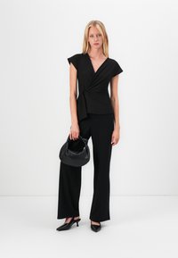 Haut noir enveloppant à manches courtes, le tissu tombe au niveau de la taille. Associé à un pantalon noir à jambes larges et un sac à main noir. Talons aiguilles.