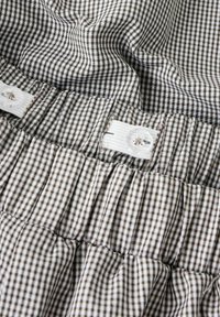 Artimųjų planas su rudai balta languota medžiaga, su reguliuojamu baltu elastingu diržu ir skaidriu plastiku mygtuku.