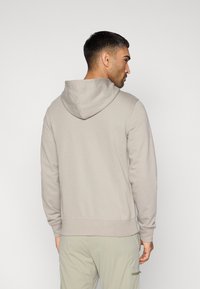 Ανοιχτό γκρι φούτερ με κουκούλα από απαλό ύφασμα, με κορδόνι στη κουκούλα, ριμπ μανσέτες και ευθεία τελείωμα. Διακριτικός σχεδιασμός χωρίς ραφές στην πλάτη.