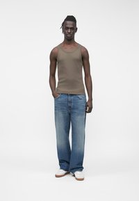 Tanktop in olijfgroen, gecombineerd met loszittende lichtblauwe jeans en witte sneakers. Soepele stof, casual ontwerp, ontspannen silhouet.